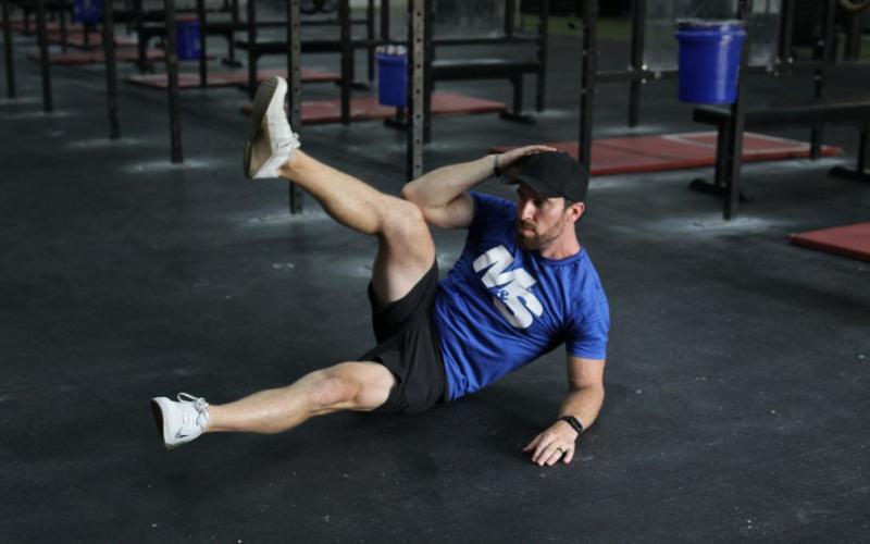 Fit man doing side crunches with leg lift in the gym. 