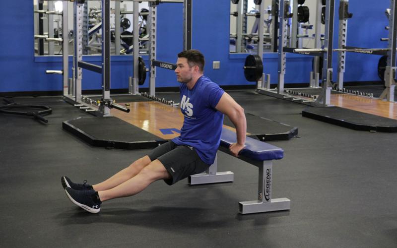 Fit man doing a single bench dip in the gym.
