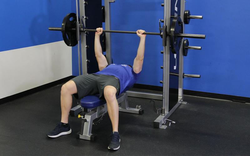 Fit man doing a smith machine bench press in the gym.