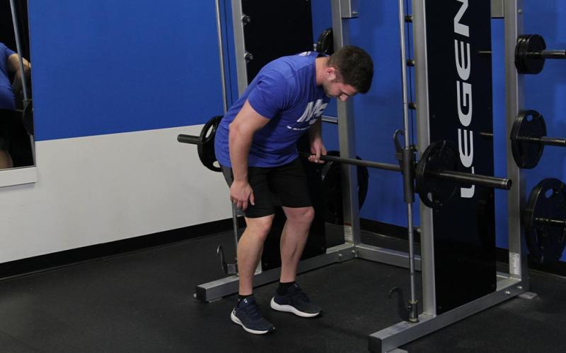 Fit man doing a one-arm row on the smith machine in the gym.