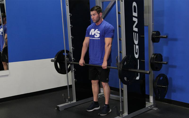 Fit man doing a smith machine stiff leg deadlift in the gym.