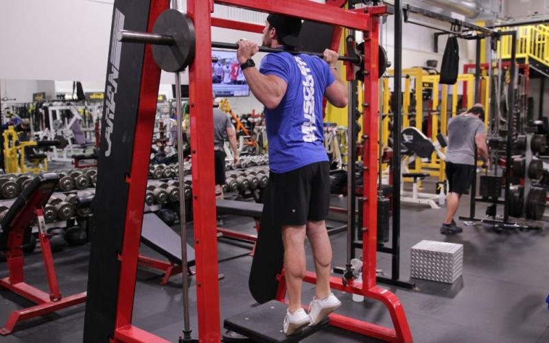 Fit man doing a Smith Machine Calf Raise with toes pointed in.