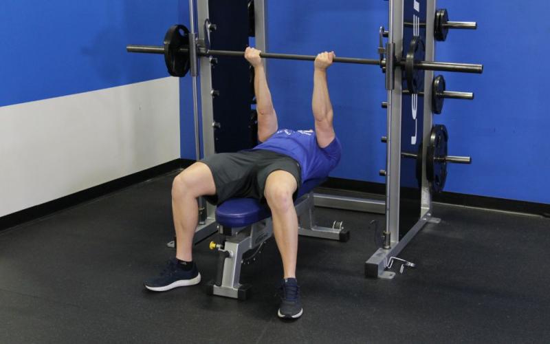 Fit man doing a smith machine reverse close grip bench press in the gym.