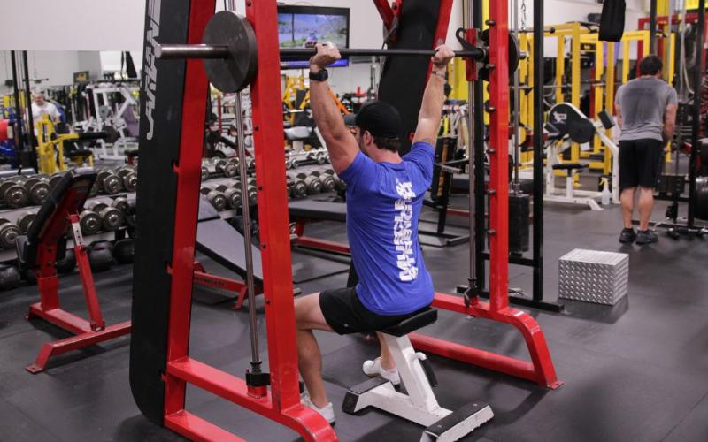 Fit man doing a Smith Machine Shoulder Press Behind-The-Neck in the gym.
