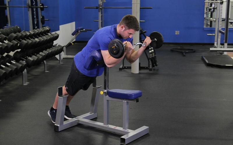 Fit man doing a spider curl in the gym.