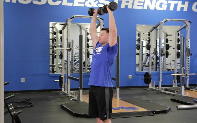 Fit man doing a standing arnold press in the gym.