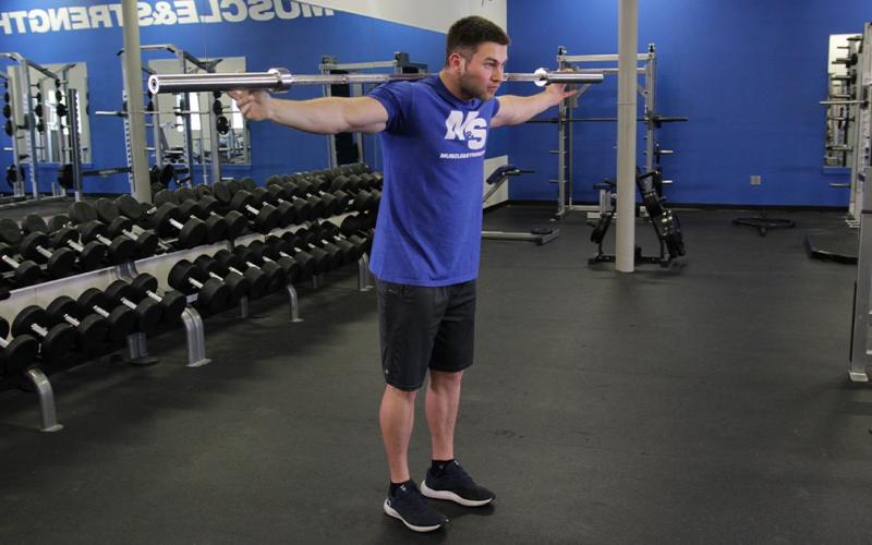 Fit man doing a standing barbell calf raise on the floor in the gym.