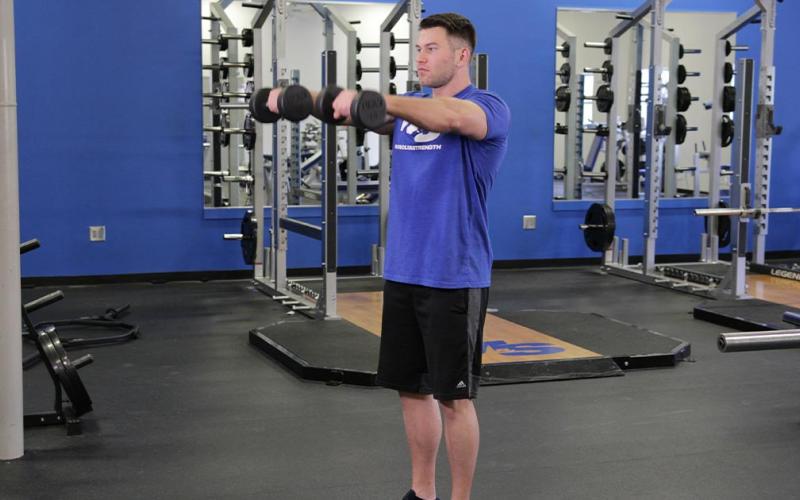 Fit man doing a standing dumbbell front raise in the gym.