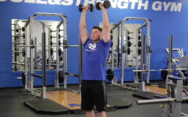Fit man doing a standing dumbbell shoulder press in the gym.