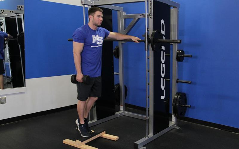 Fit man doing a standing one-leg calf raise while holding a dumbbell.