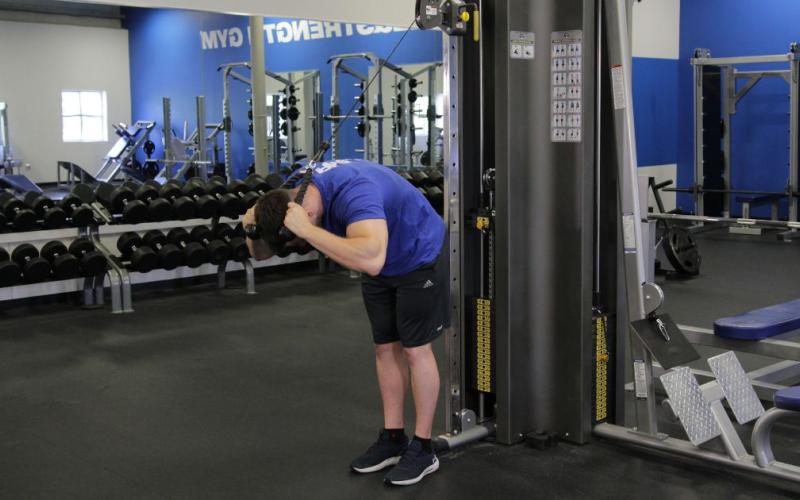 Fit man doing a standing cable crunch in the gym.