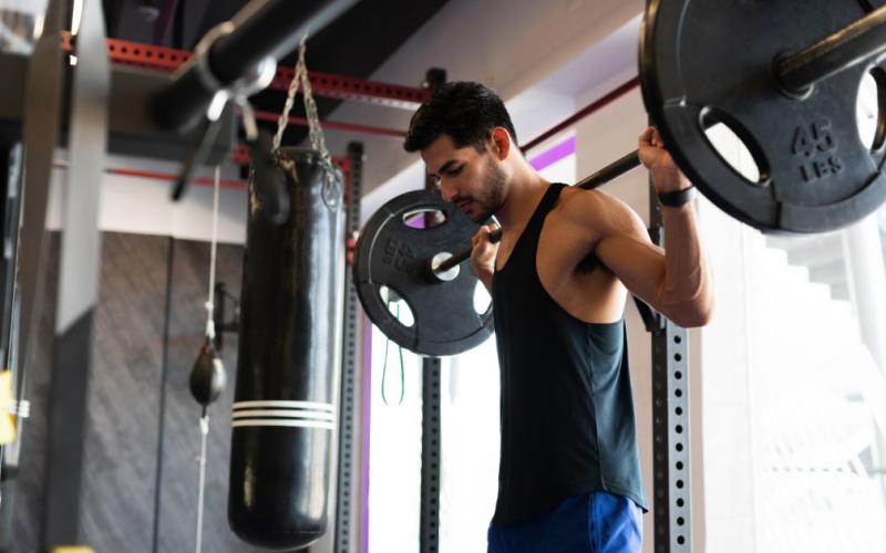 Strong latino man doing barbell back squats in the gym.