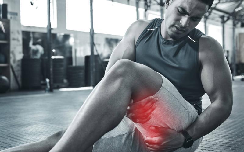 Muscular man in the gym with tendonitis pain is his leg