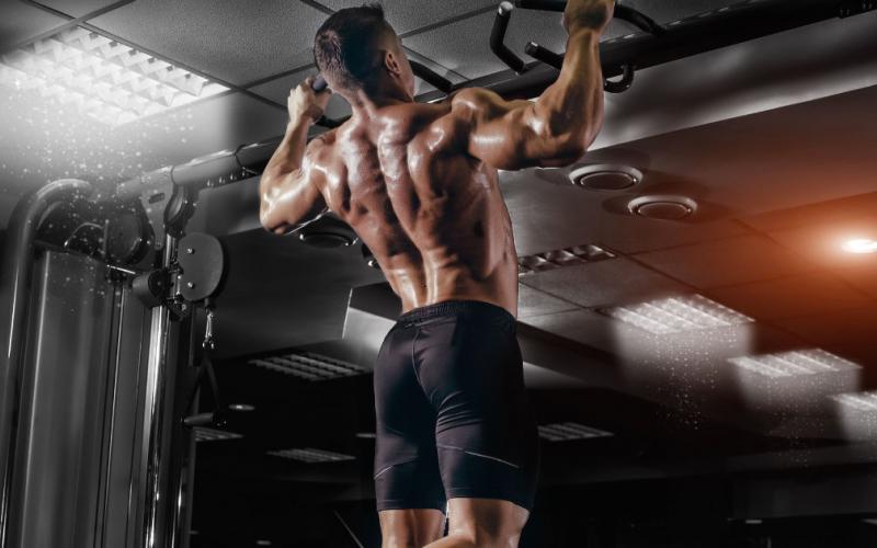 Muscular man in black shorts performing pull-ups in gym