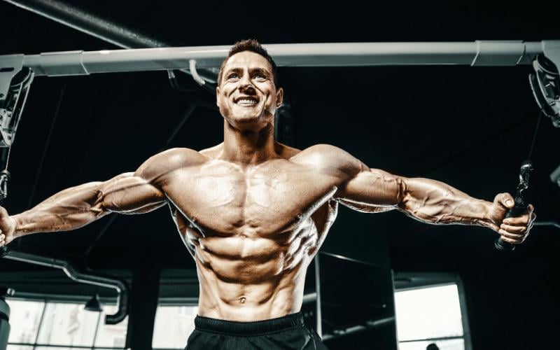 Shirtless, muscular man doing machine cable flys.