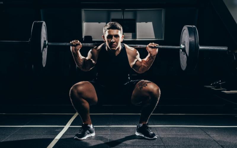 Man doing barbell back squat in gym.