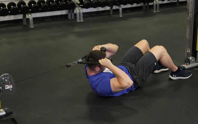 Fit man doing a twisting lying cable crunch in the gym.