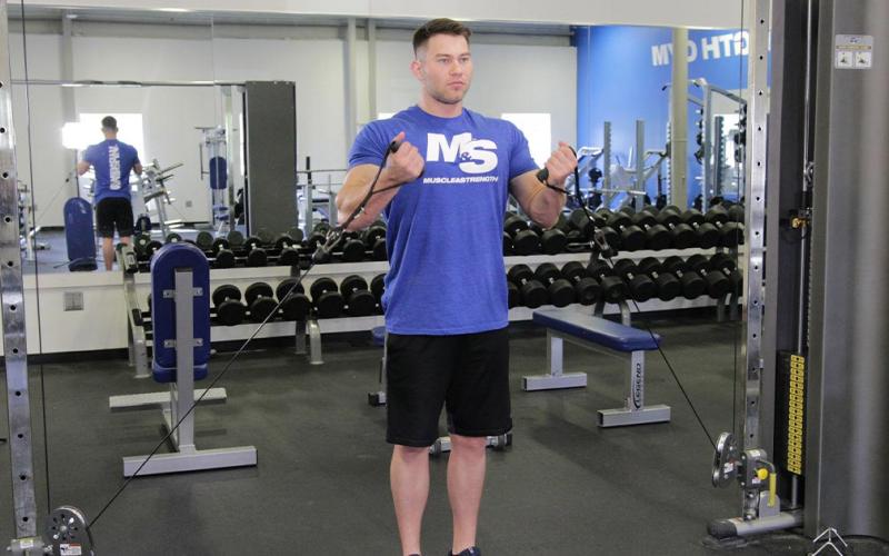 Fit man doing a two-arm low pulley cable curl in the gym.