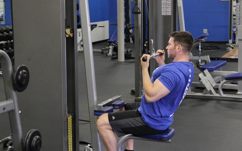 Fit man doing an underhand close grip lateral pulldown in the gym.