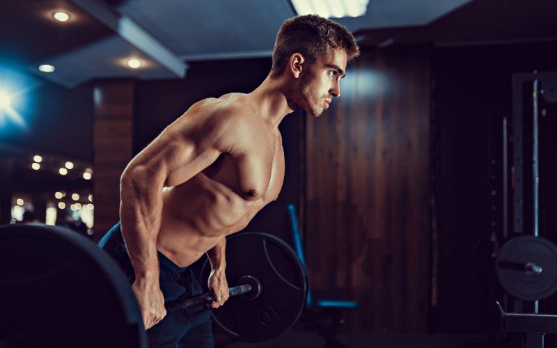 Muscular man doing barbell rows in gym setting.