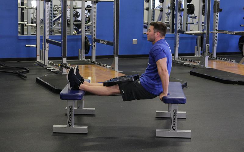Fit man doing weighted bench dips in the gym.