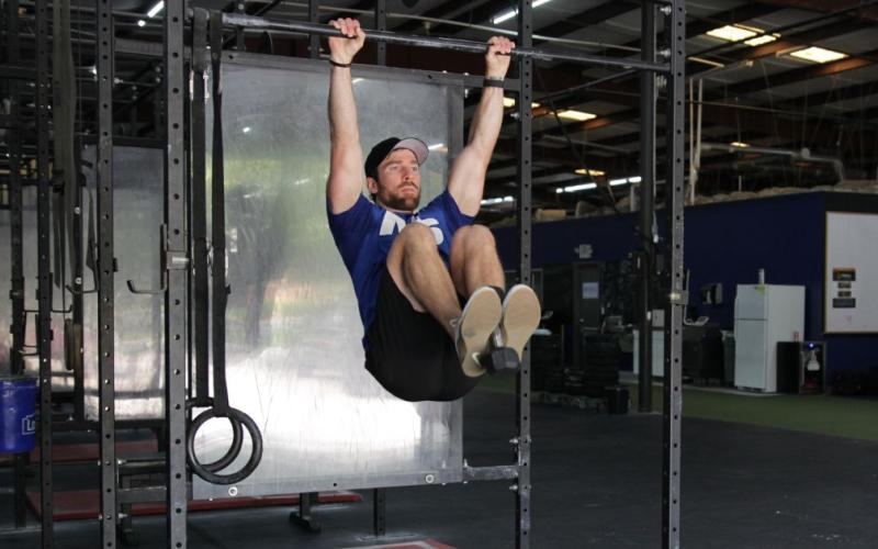 Fit man doing weighted hanging knee raises in the gym.