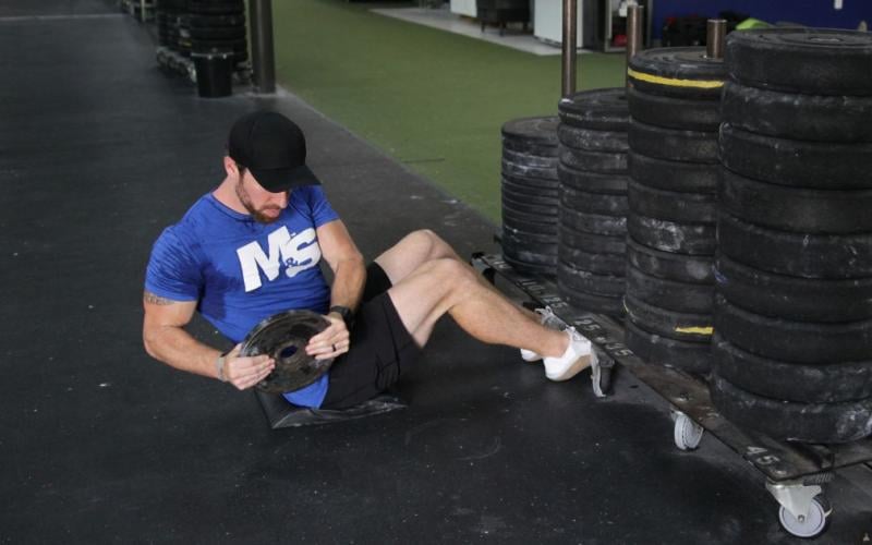 Fit man doing Weighted Russian Twists in the gym.