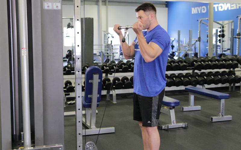 Fit man doing a wide grip cable curl in the gym.