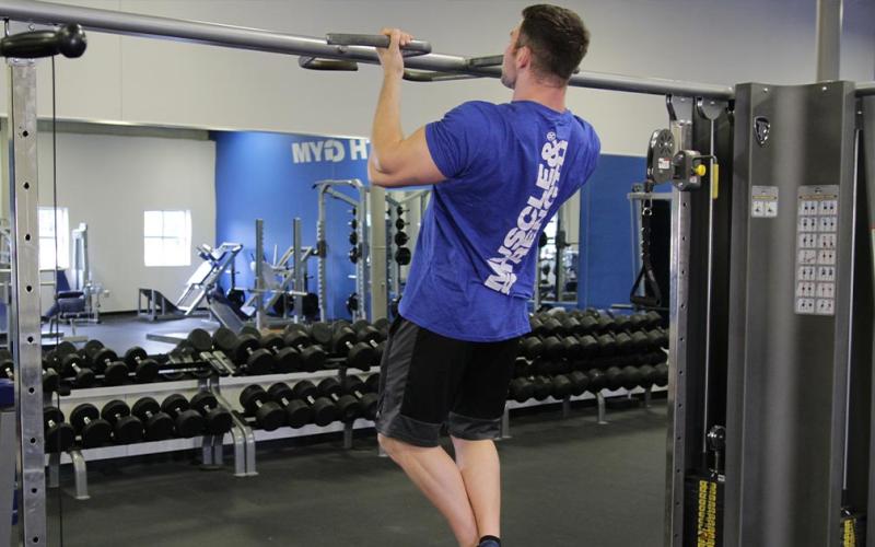 Fit man doing a wide grip chin up in the gym.