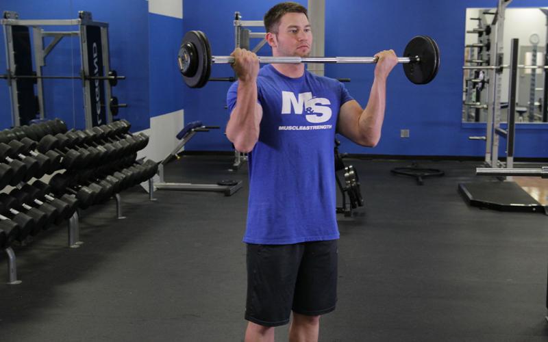 Fit man doing a wide grip standing barbell curl in the gym.
