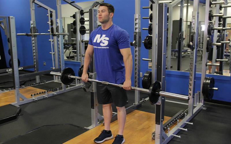 Fit man doing a wide grip barbell upright row in the gym.