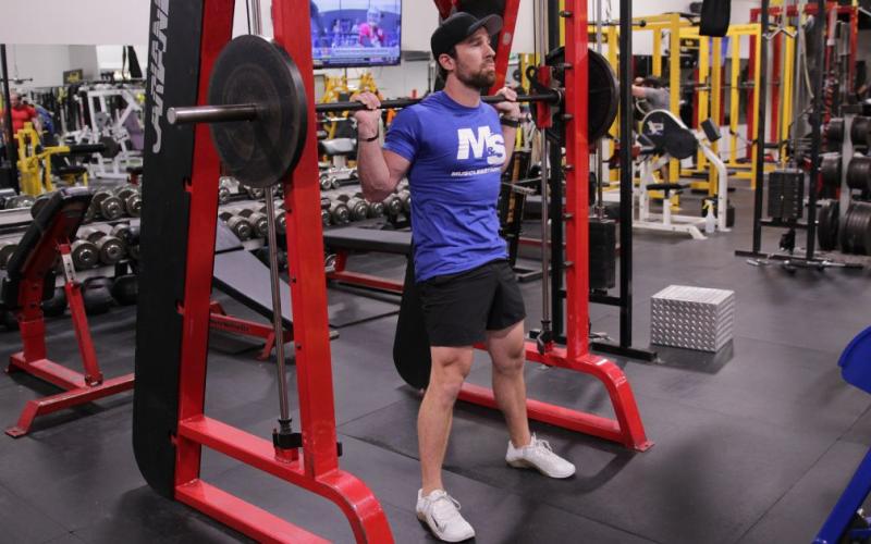Fit man doing a wide stance smith machine squat in the gym.