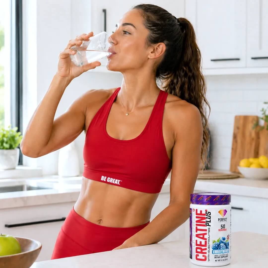 Woman in red activewear drinking a refreshing glass of water in her kitchen next to Frostberry Ultra Creatine Plus