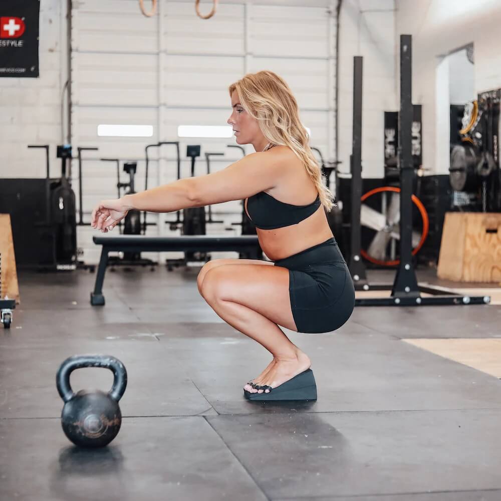 Female athletes performing air squats in gym using mobility wedge and toe spacers